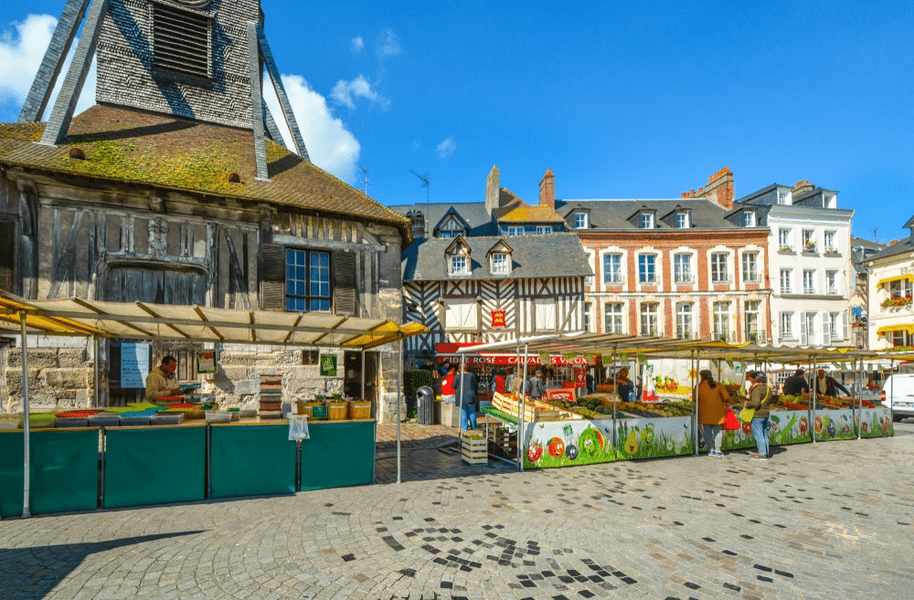 Marktkraampjes op een plein in Honfleur omringd door gekleurde huizen.